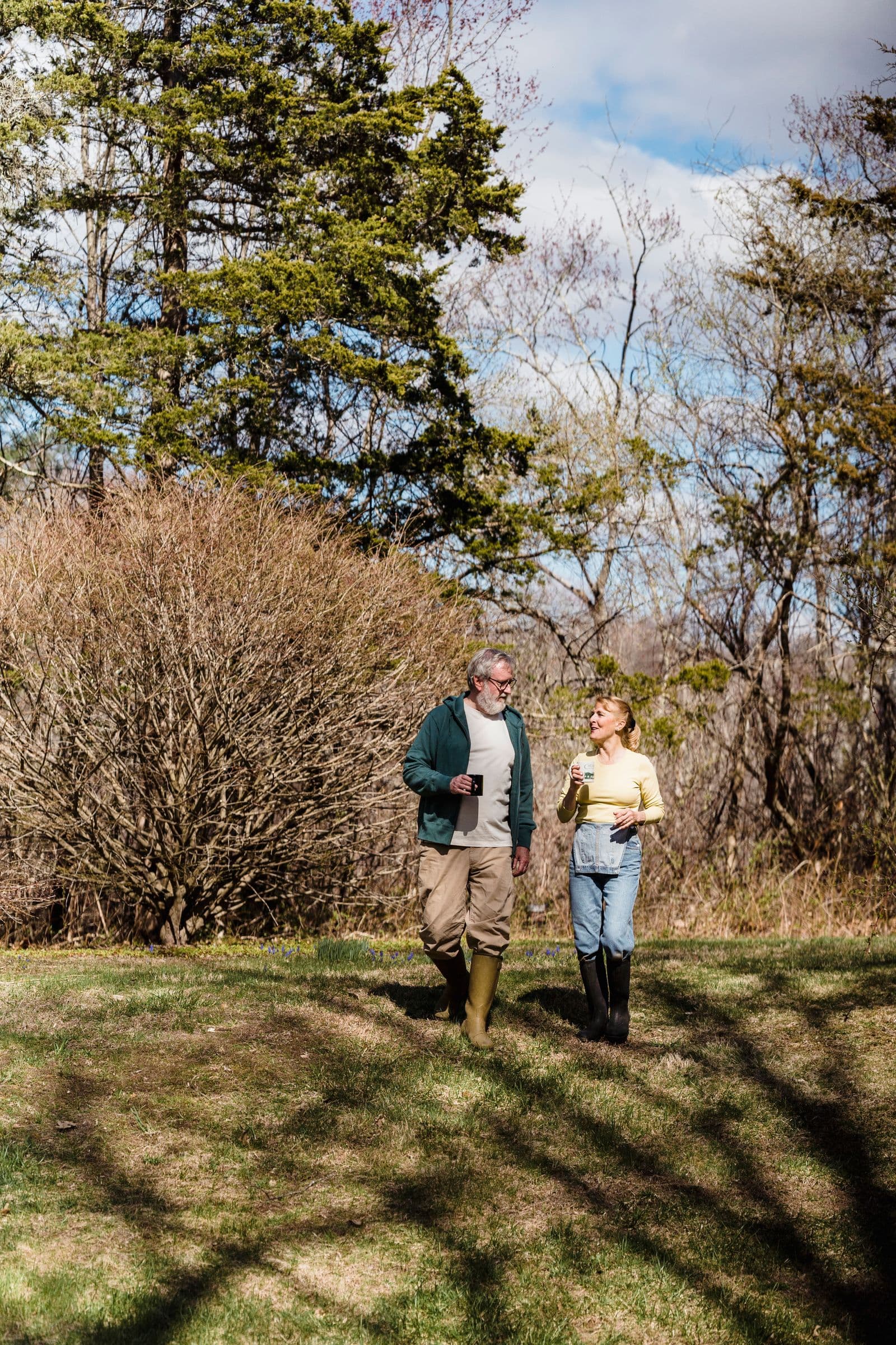 An older couple walks together across a grass field.